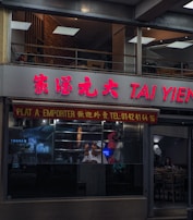 A street view of a restaurant with signage in both Chinese and English. The name 'TAI YIEN' is prominently displayed in red letters. The window showcases what appears to be roast meats on display, hinting at it being a Chinese barbecue restaurant. Interior seating is visible through the glass, with a cozy atmosphere inside.