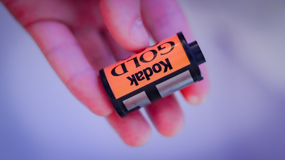 a hand holding a small orange and black battery
