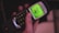 A hand holding a classic mobile phone with a green backlit screen displaying a menu. The phone has a physical keypad with numbers and icons, and the screen shows options like 'Services' and 'Home'. The device has a retro design with an antenna.