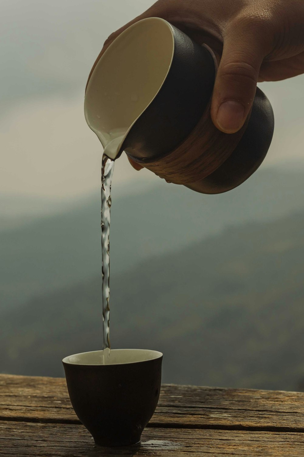 a person pouring water into a cup on top of a wooden table