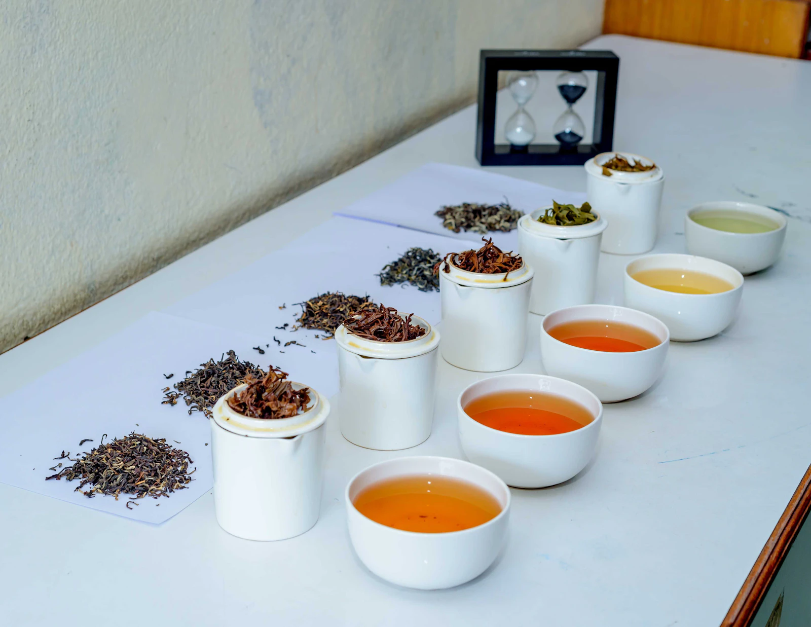 White lidded tasting cups, heaps of dry leaf and bowls of liquor from pale gold to copper on a tasting table