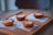 Four golden-brown pastries are neatly arranged on a wooden tray, each placed on a square napkin. The pastries have a slightly caramelized crust with scattered sugar crystals visible on their tops. The setting conveys a warm, cozy atmosphere with natural lighting gently highlighting the textures of the food and tray.