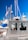 A metal emergency boat equipped with antennas and communication devices docked at a marina with several sailboats in the background. The boat has windows and is labeled with 'Emergencies Urgences' on its side. A flag is attached to one of the boat's antennas.