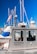 A metal emergency boat equipped with antennas and communication devices docked at a marina with several sailboats in the background. The boat has windows and is labeled with 'Emergencies Urgences' on its side. A flag is attached to one of the boat's antennas.