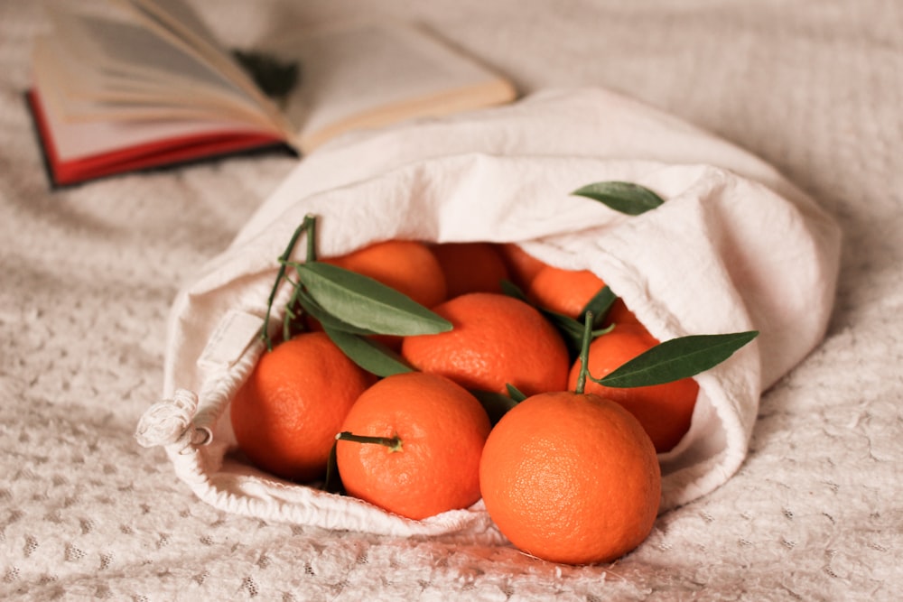 a white cloth bag filled with oranges on top of a bed