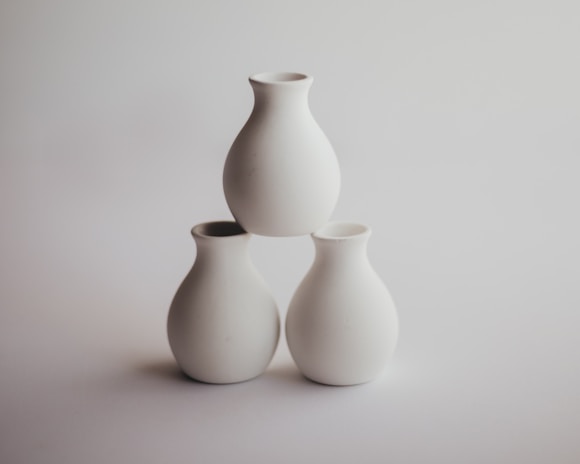 A set of three vases with varying shapes and sizes arranged as a centerpiece on a dining table with soft natural light.