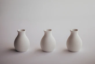 A set of elegant, simple ceramic vases arranged on a white shelf.