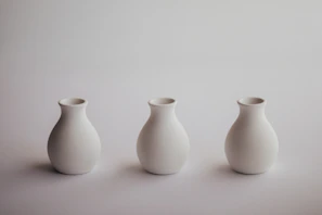 A set of elegant, simple ceramic vases arranged on a white shelf.