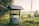 A rustic water well with a wooden roof, surrounded by lush greenery and a serene rural landscape. The setting sun casts a warm glow over the scene, enhancing the peaceful ambiance.