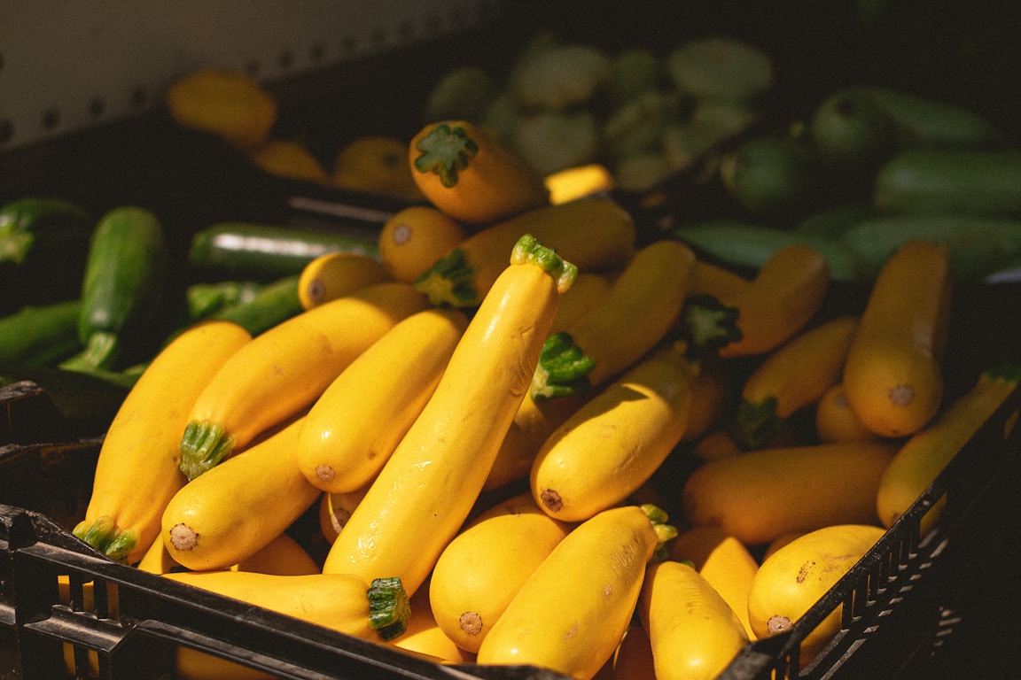 A crate filled with fresh yellow zucchini and green peppers at a market