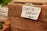 A handwritten note attached to a wooden crate with tape reads 'Cash is preferred! - thanks!!'. The scene appears to be part of a market setting, with fresh greenery visible in the background, likely indicating some produce or herbs.