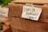 A handwritten note attached to a wooden crate with tape reads 'Cash is preferred! - thanks!!'. The scene appears to be part of a market setting, with fresh greenery visible in the background, likely indicating some produce or herbs.