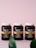 Three brown bottles with white caps are placed side by side on a soft pink surface. The label on the bottles reads 'FJORD STRONG OMEGA-3' and features an image of a fish. The packaging design includes a horizontal orange stripe and some text in a foreign language. Partially blurred green leaves are visible at the bottom of the image.