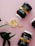 Several jars labeled 'Fjord' containing omega-3 capsules are arranged on a pink surface. The jars are dark with white caps, while the labels are predominantly yellow and black. Some capsules are placed in a small dish and scattered around. Green leaves serve as an accent in the composition.