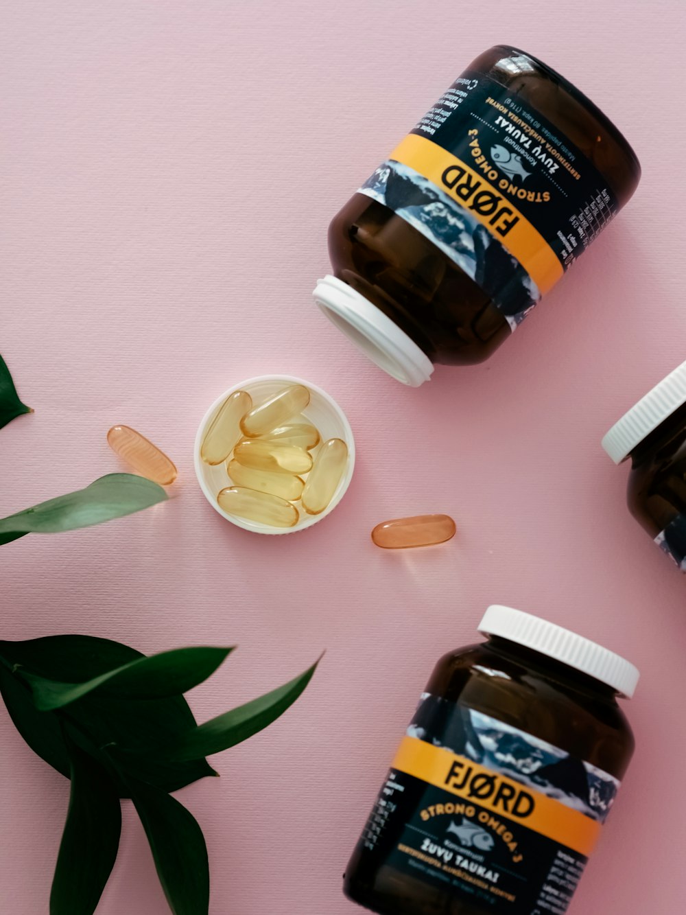 three bottles of fish oil sitting on top of a pink surface