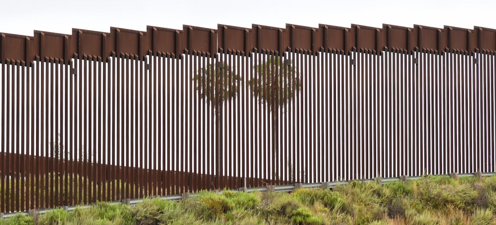 a tall metal fence next to a lush green hillside