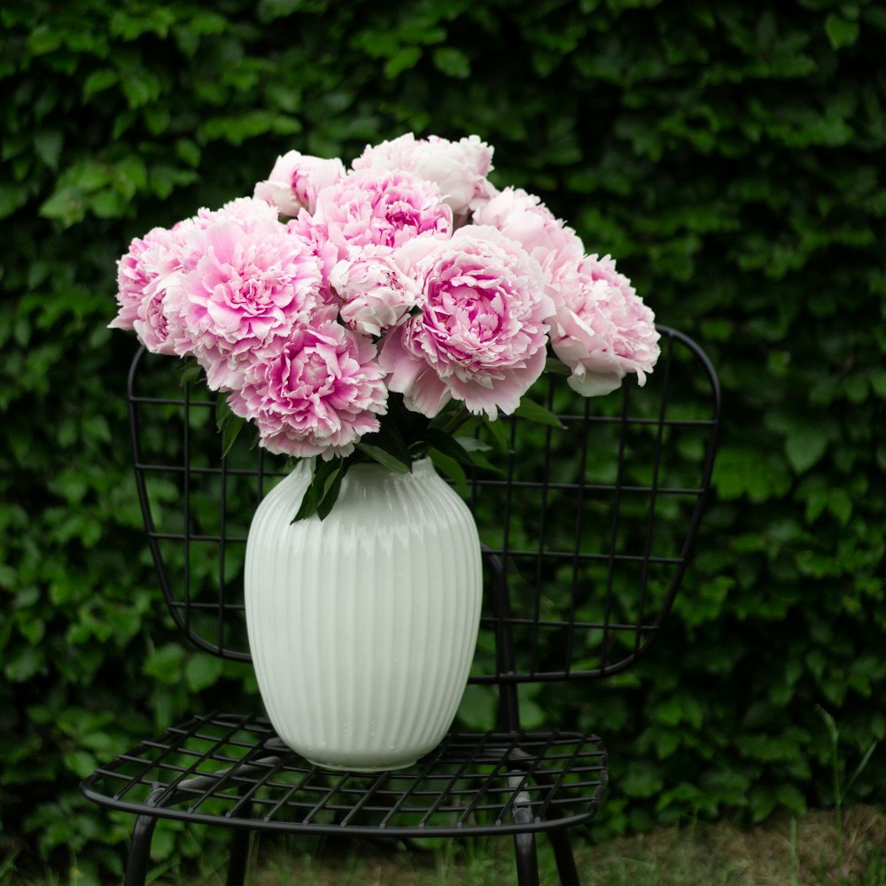 a white vase filled with pink flowers sitting on a chair