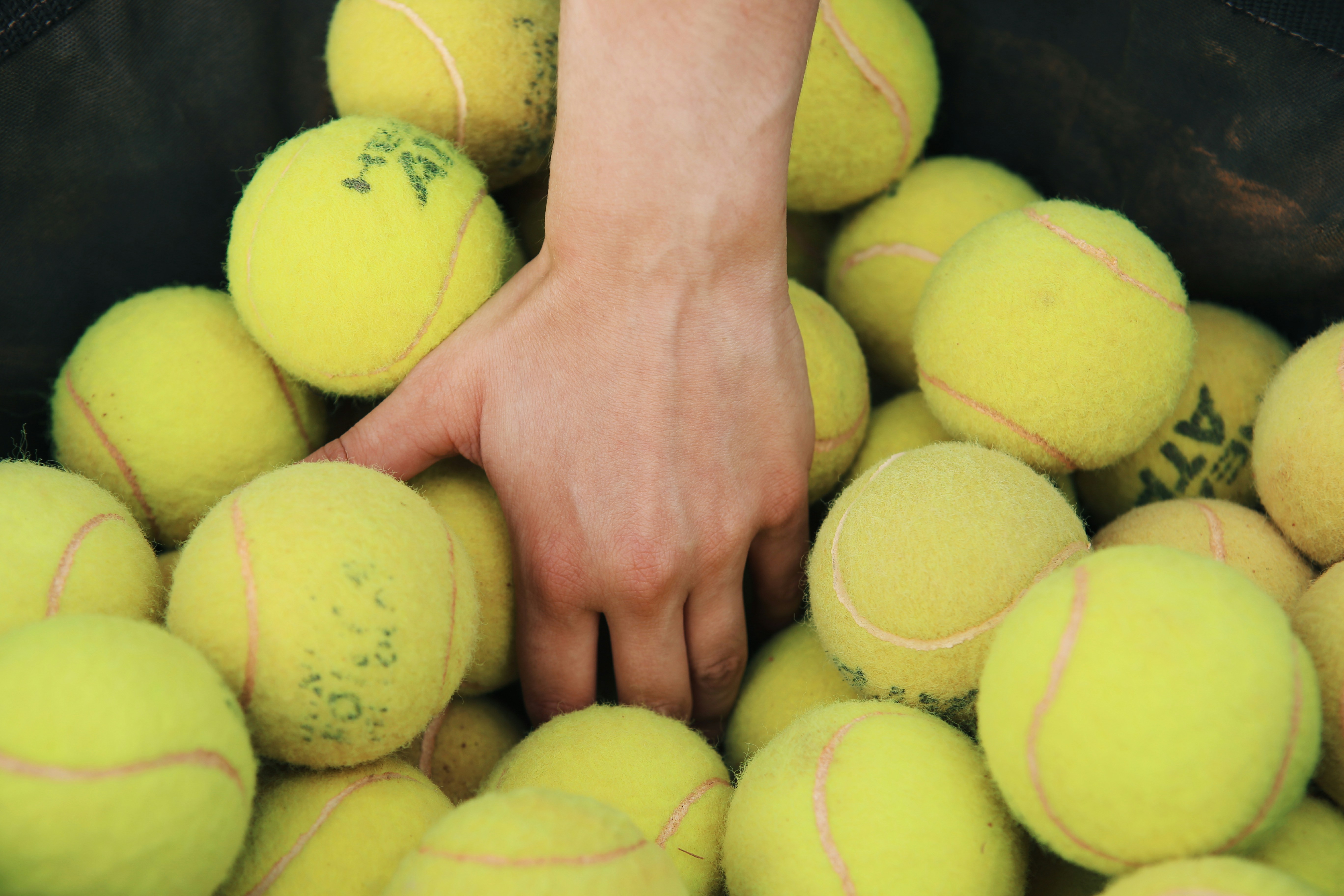 a person reaching for a tennis ball in a bin