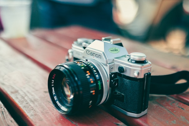 Close-up of a sleek mirrorless camera with a leather strap resting on a wooden table.