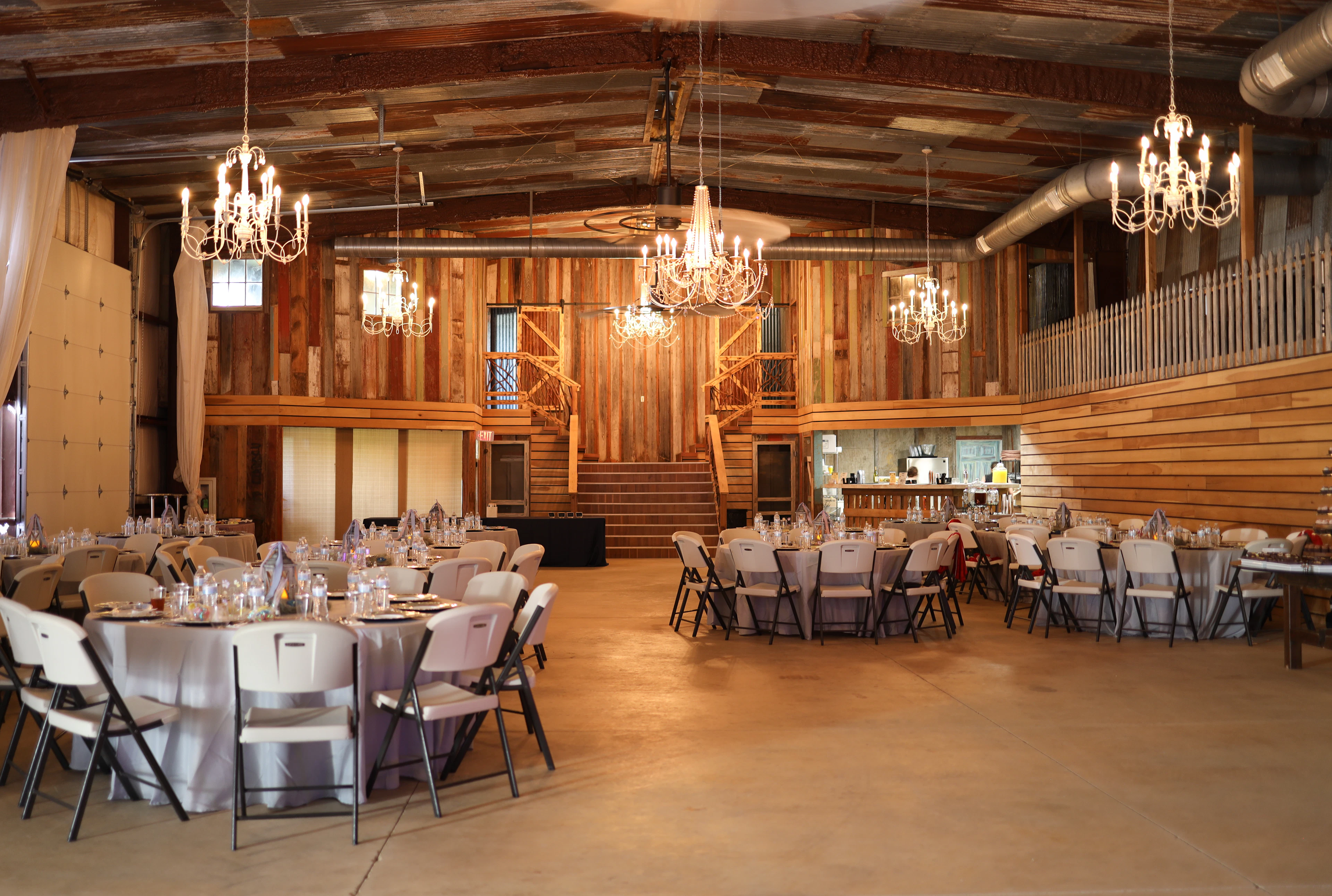 Rustic barn interior with chandeliers, string lights and round tables