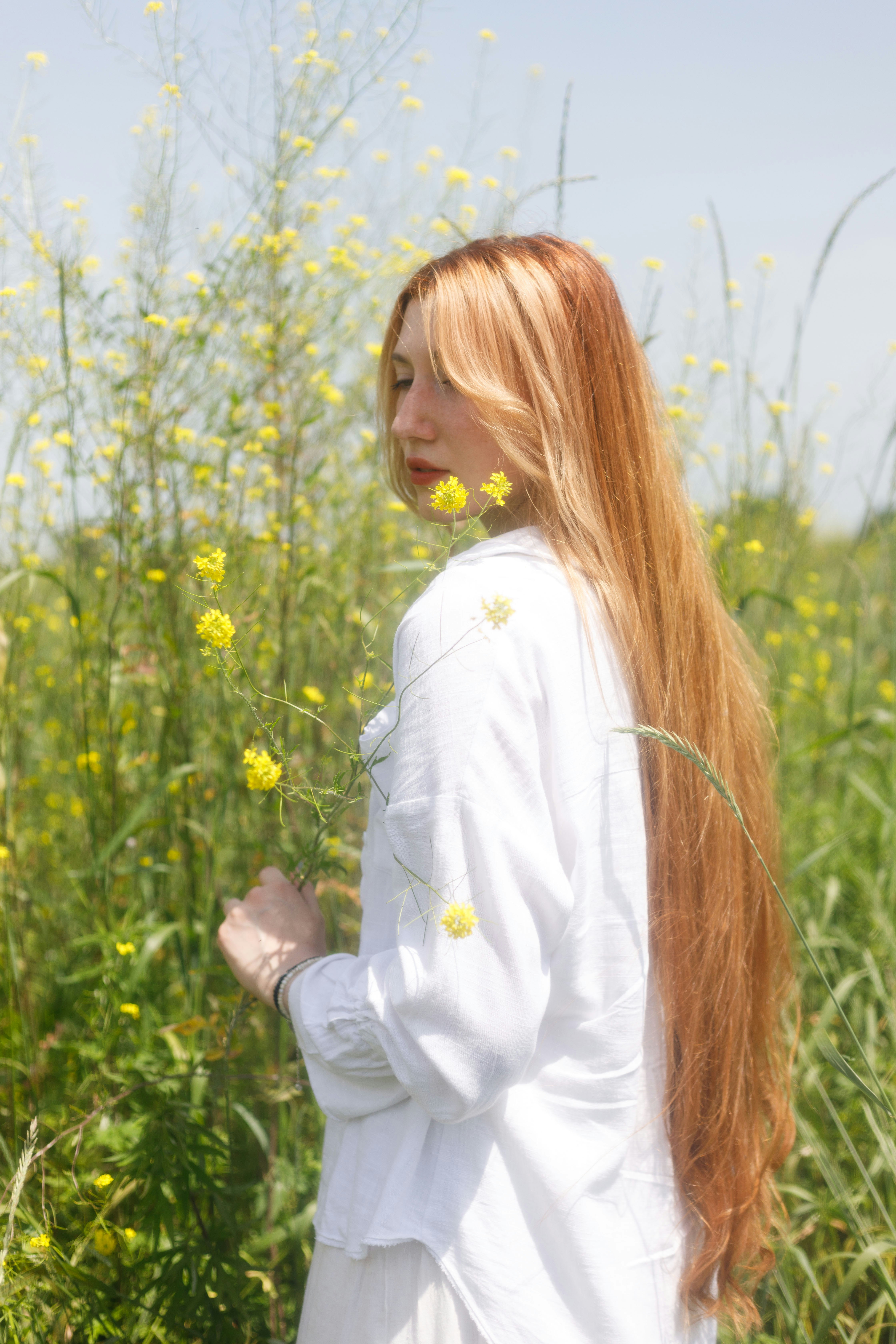 a woman with long red hair standing in a field of flowers