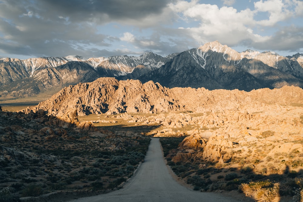 a dirt road surrounded by mountains under a cloudy sky