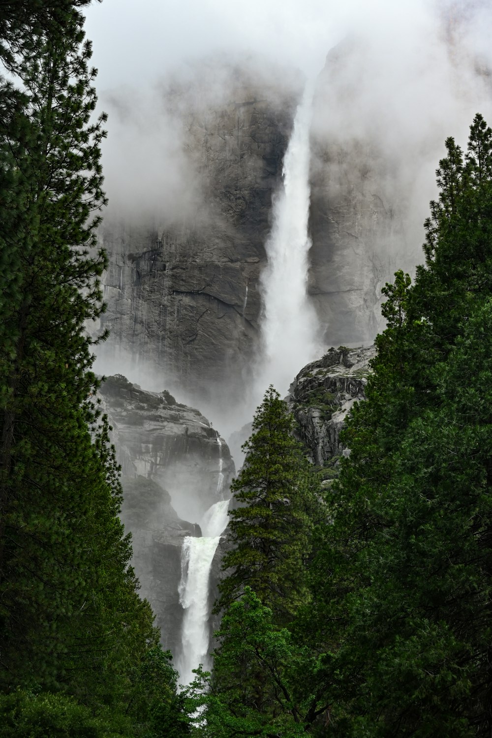 a tall waterfall surrounded by trees and fog