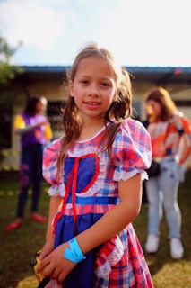 a little girl in a plaid dress holding a cell phone