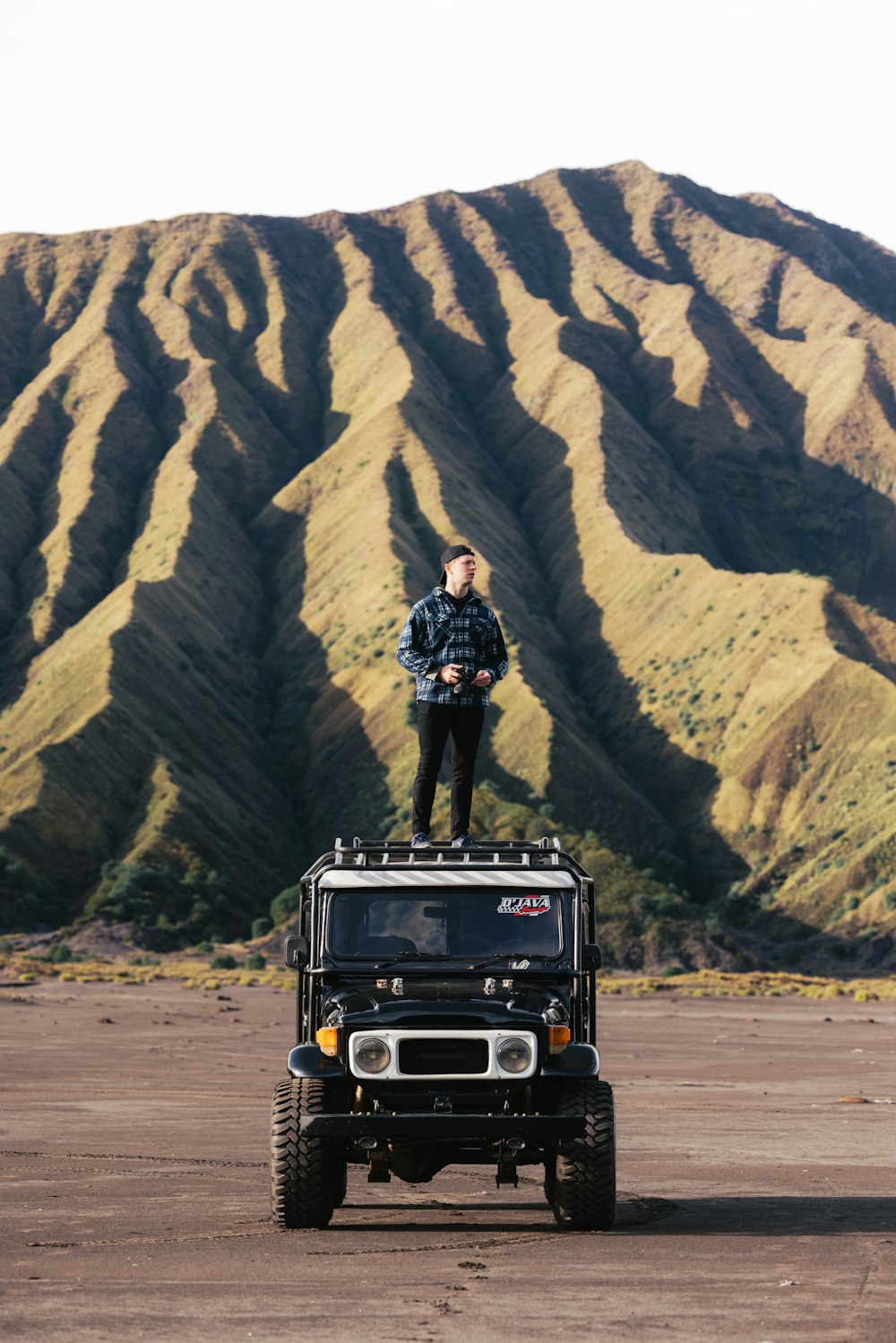 a man standing on top of a jeep in front of a mountain