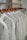 A row of white shirts neatly arranged on wooden hangers in a closet or store setting. The shirts have a simple design, creating a clean and organized appearance.