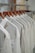 A row of white shirts neatly arranged on wooden hangers in a closet or store setting. The shirts have a simple design, creating a clean and organized appearance.