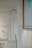A minimalist setting featuring an elegant, sleeveless white dress hanging on a wooden hanger against a speckled wall. Below it, several garments in similar light hues are displayed on hangers, creating a serene and harmonious arrangement.