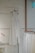 A minimalist setting featuring an elegant, sleeveless white dress hanging on a wooden hanger against a speckled wall. Below it, several garments in similar light hues are displayed on hangers, creating a serene and harmonious arrangement.