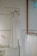 A minimalist setting featuring an elegant, sleeveless white dress hanging on a wooden hanger against a speckled wall. Below it, several garments in similar light hues are displayed on hangers, creating a serene and harmonious arrangement.