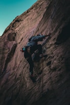 A climber ascending a rugged rock face with a panoramic view of the Colombian Andes.
