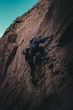 A climber ascending a rugged rock face with a panoramic view of the Colombian Andes.