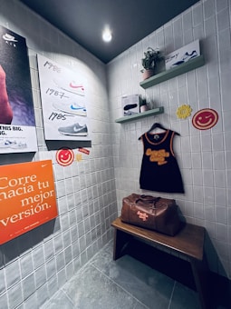 A small retro-themed display with a focus on athletic apparel and shoes. The walls feature a series of posters showcasing various Nike shoes from different years. A black gym tank top and a brown leather gym bag are prominently positioned on a wooden bench. There are decorative elements like potted plants on wall-mounted shelves and smiley face icons. The environment has a nostalgic and sporty atmosphere.