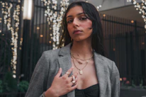 Model wearing layered necklaces and bold earrings against a city backdrop.