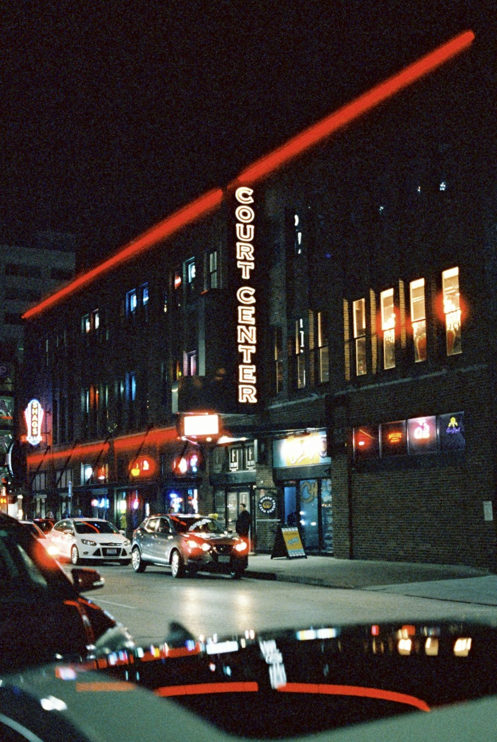 a city street at night with cars parked on the side of the street