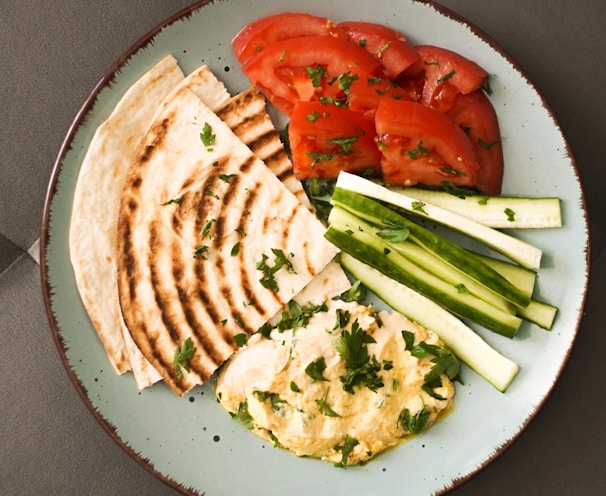 a plate of food that includes pita bread, tomatoes and cucumbers