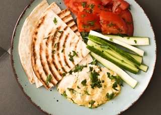 a plate of food that includes pita bread, tomatoes and cucumbers