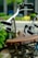 The image focuses on a vintage bicycle seat with a brown leather surface and metal springs, prominently featuring the brand name 'Lepper'. The background is softly blurred, showing hints of greenery and an urban setting.