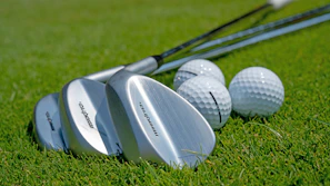Close-up of a shiny new golf club head resting on fresh green grass under sunlight