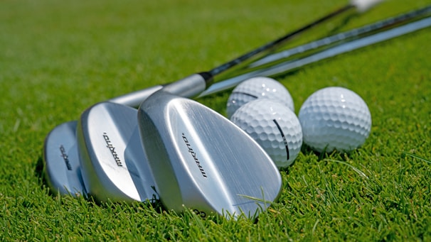 Close-up of golf clubs resting on soft grass at dawn.