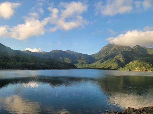 A serene landscape showing a calm lake reflecting green hills under a clear blue sky.