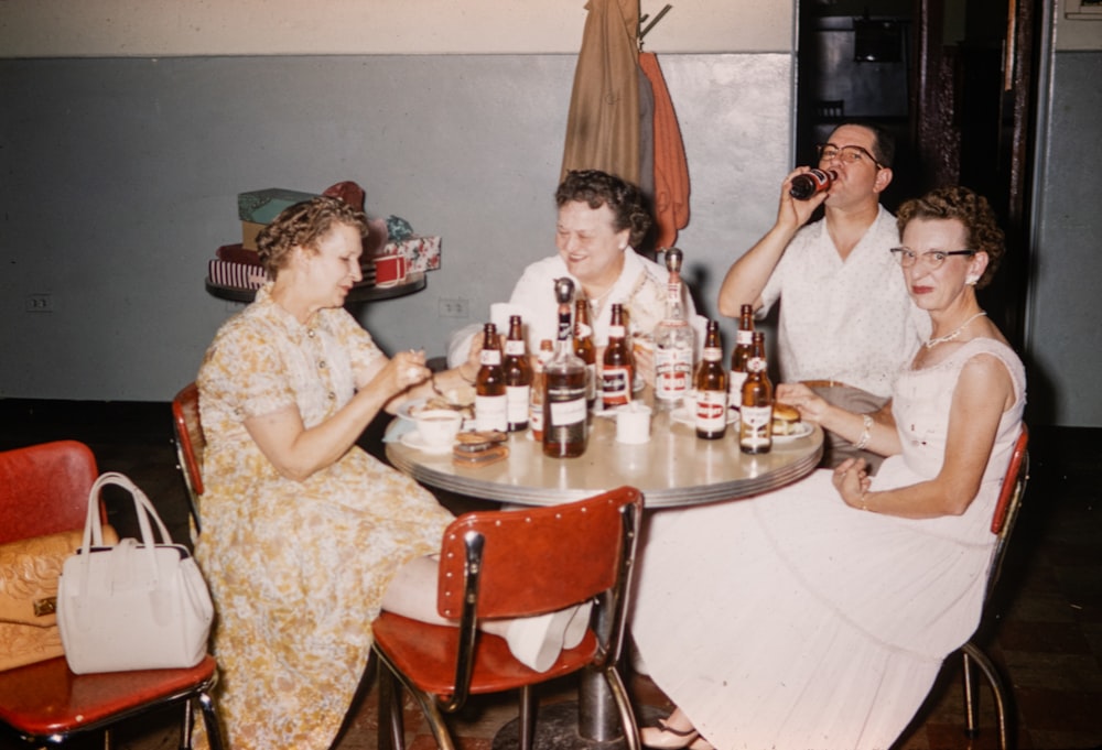 a group of people sitting around a table with bottles of beer