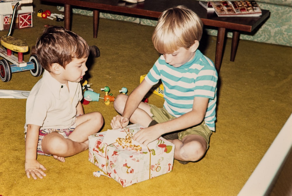 two young boys sitting on the floor playing with a gift