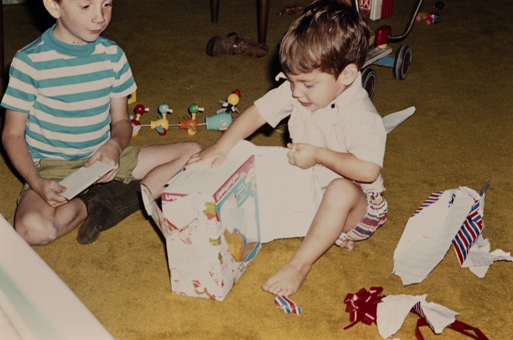 two young boys sitting on the floor reading a book