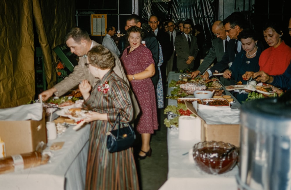 a group of people standing around a table filled with food