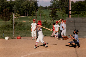 Young players practicing batting drills under the guidance of a coach on a sunny day
